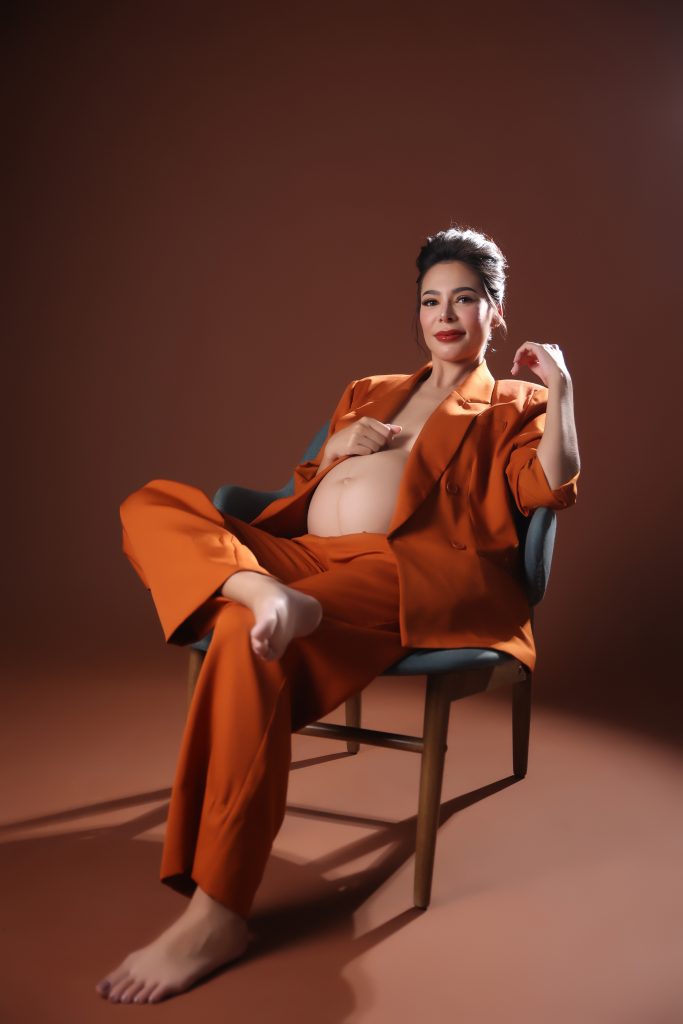 emma rueda ayala maternity photoshoot with brown background wearing an orange oversized suit