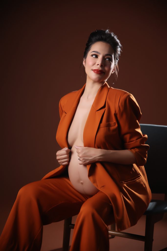 emma rueda ayala maternity photoshoot with brown background wearing an orange oversized suit
