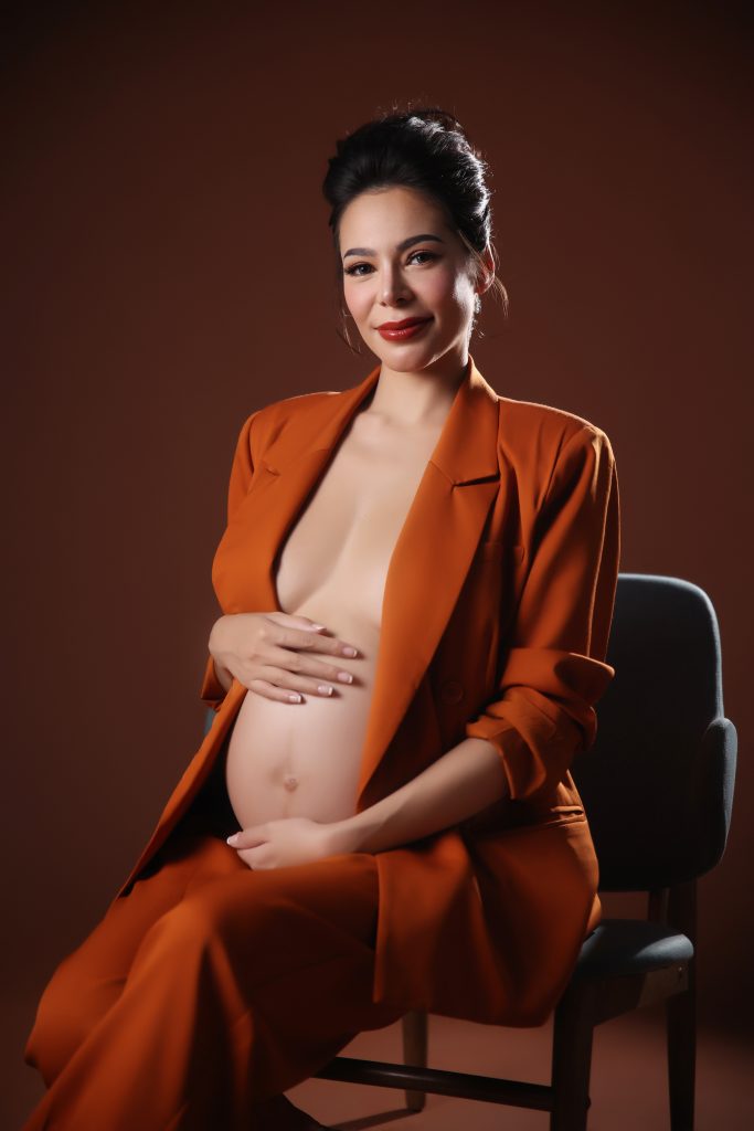 emma rueda ayala maternity photoshoot with brown background wearing an orange oversized suit