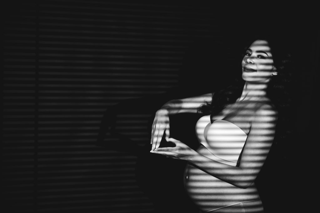 emma rueda ayala maternity photoshoot with black background making a heart shaped-silhoutte 