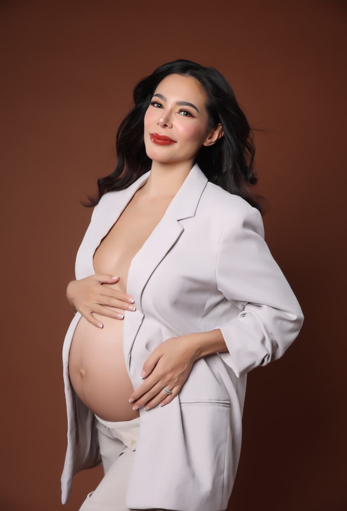 emma rueda ayala maternity photoshoot with brown background wearing an white oversized suit