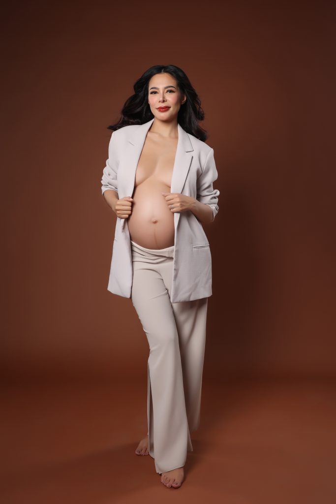 emma rueda ayala maternity photoshoot with brown background wearing an white oversized suit
