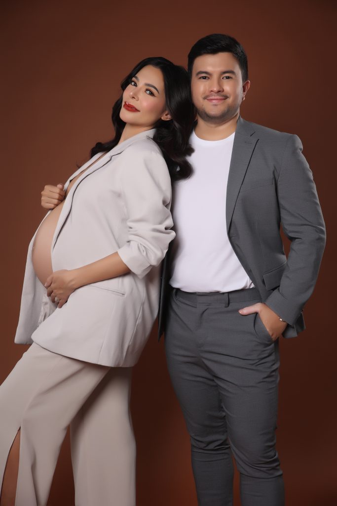 emma rueda ayala maternity photoshoot with brown background wearing an white oversized suit with husband lucho ayala wearing a grey suit