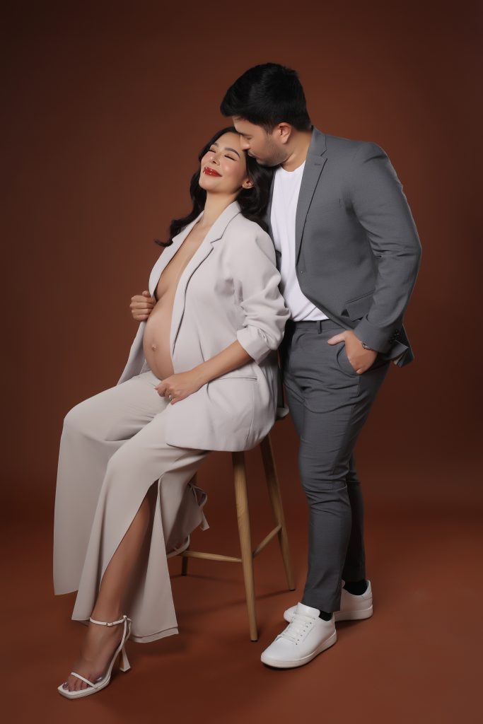 emma rueda ayala maternity photoshoot with brown background wearing an white oversized suit with husband lucho ayala wearing a grey suit