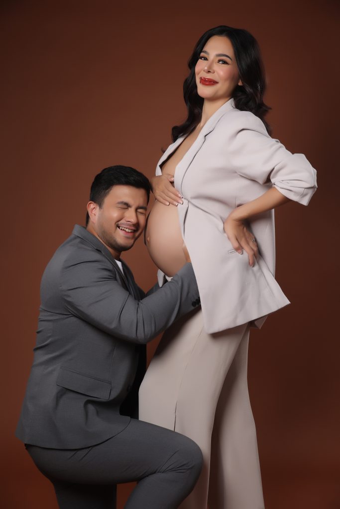 emma rueda ayala maternity photoshoot with brown background wearing an white oversized suit with husband lucho ayala wearing a grey suit